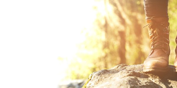 Person wearing brown hiking boots standing on a rock in sunlight.