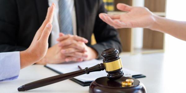 Divorce discussion with raised hand and wedding rings near gavel.