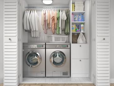 Organized laundry closet with washer, dryer, hanging clothes, and shelves of cleaning supplies.
