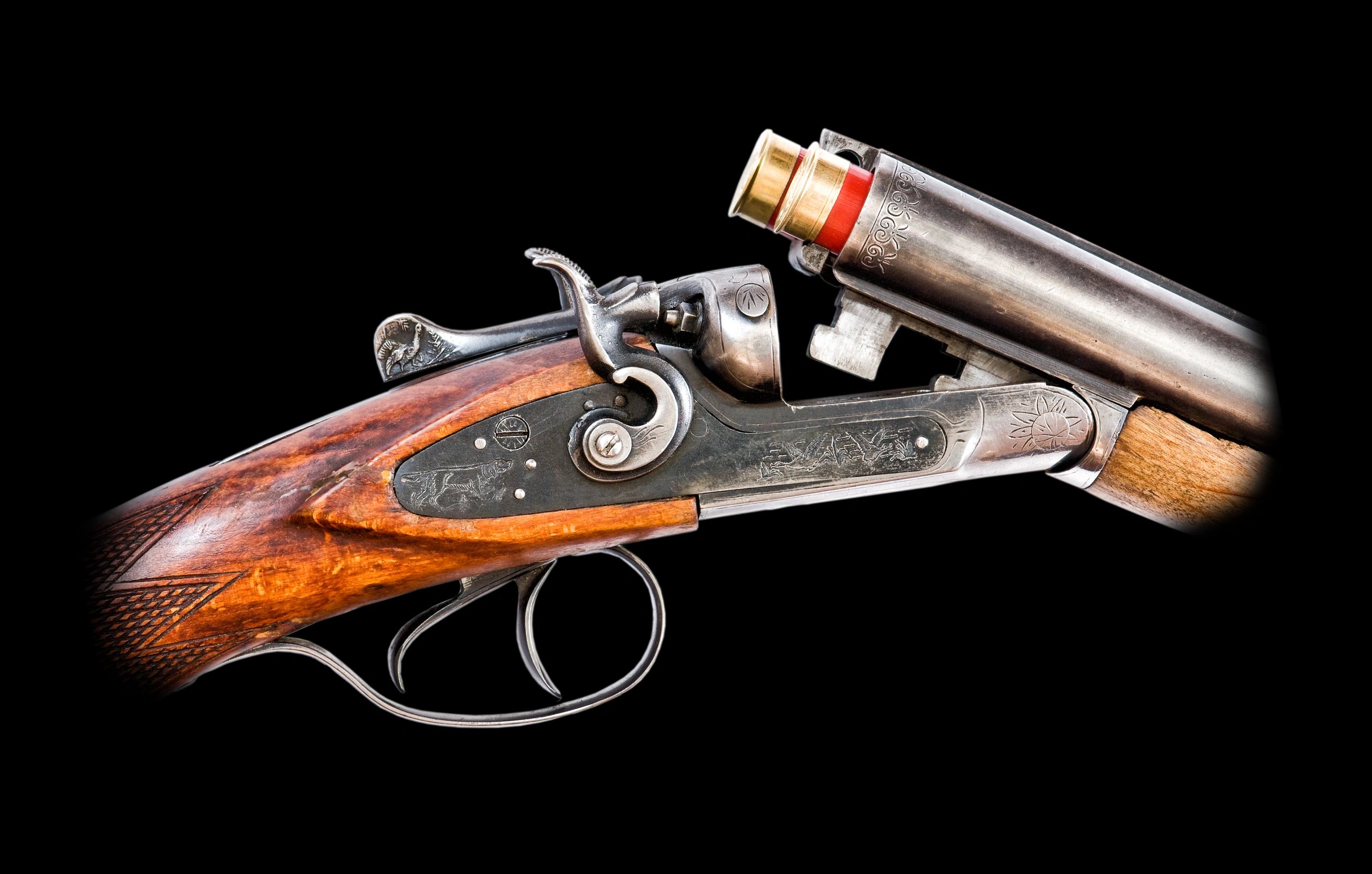 Close-up of a vintage double-barrel shotgun with wooden stock and intricate metal engravings.