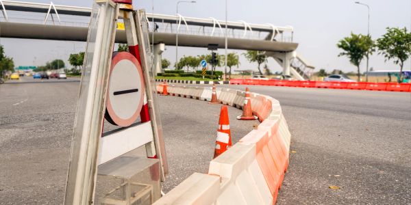 Verkeersafzetting op een weg met oranje en witte barrières en kegelhouders.