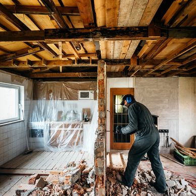 Man demolishing a brick wall during home renovation with protective gear.