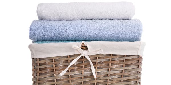 Stacked clean towels in a woven basket with cloth lining.
