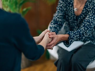 Two people holding hands in a comforting gesture during a conversation.
