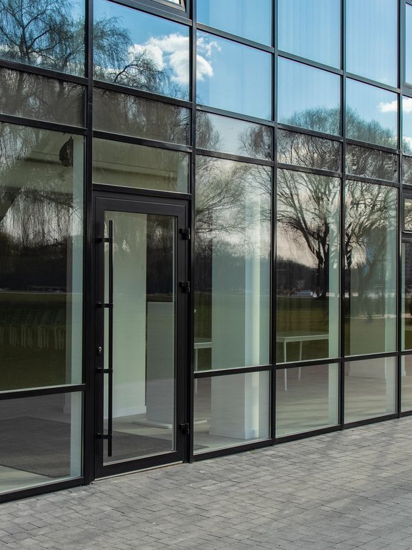 Modern glass building facade with reflections of trees and sky.