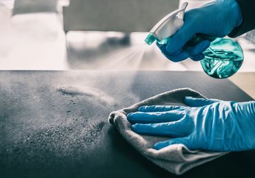 Gloved hands spraying and wiping a surface with a cloth.