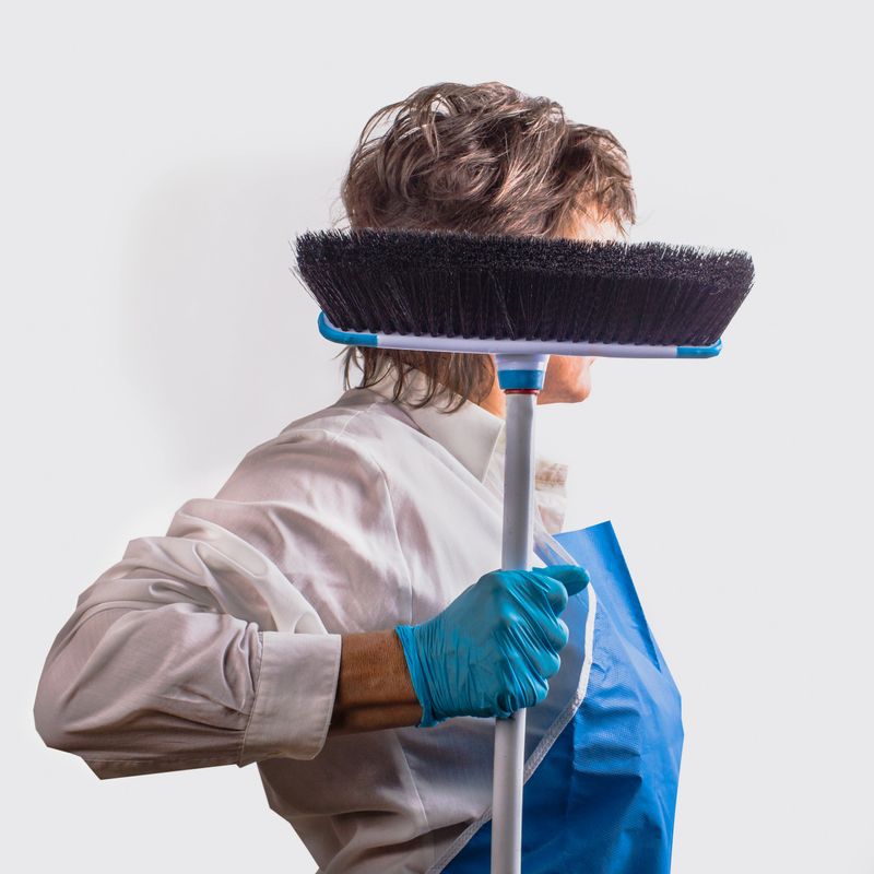 Woman  in a blue apron and latex glove with a brush in her hands is ready for thorough work.