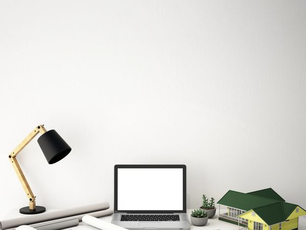 Modern workspace with architectural tools, laptop, and a house model on a clean desk.