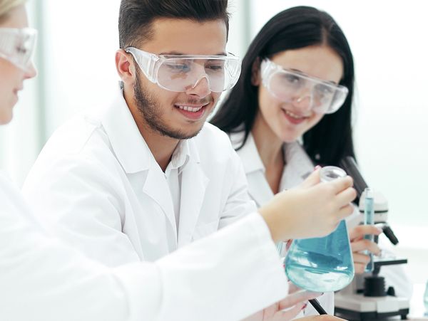 Students in lab coats conducting a chemistry experiment with safety goggles.