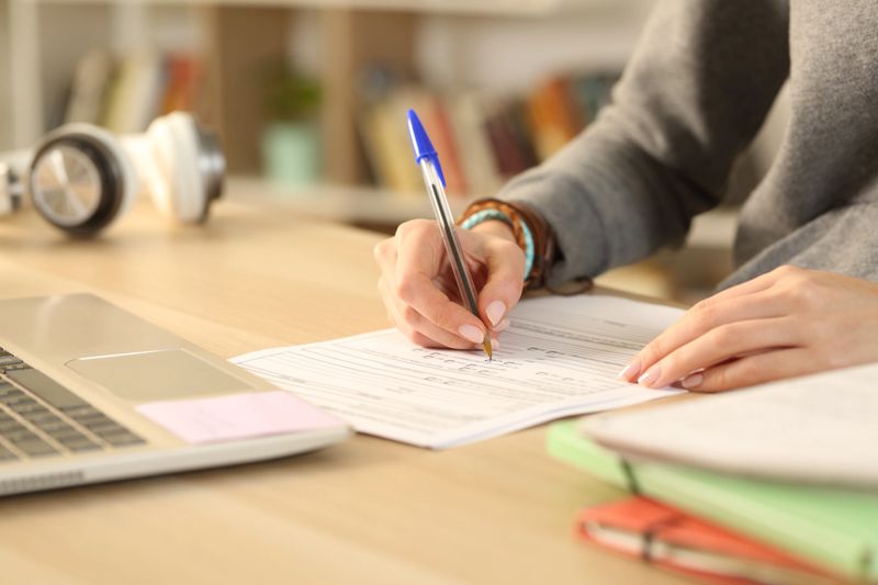Close up of student girl hands filling out form document sitting on a desk at home