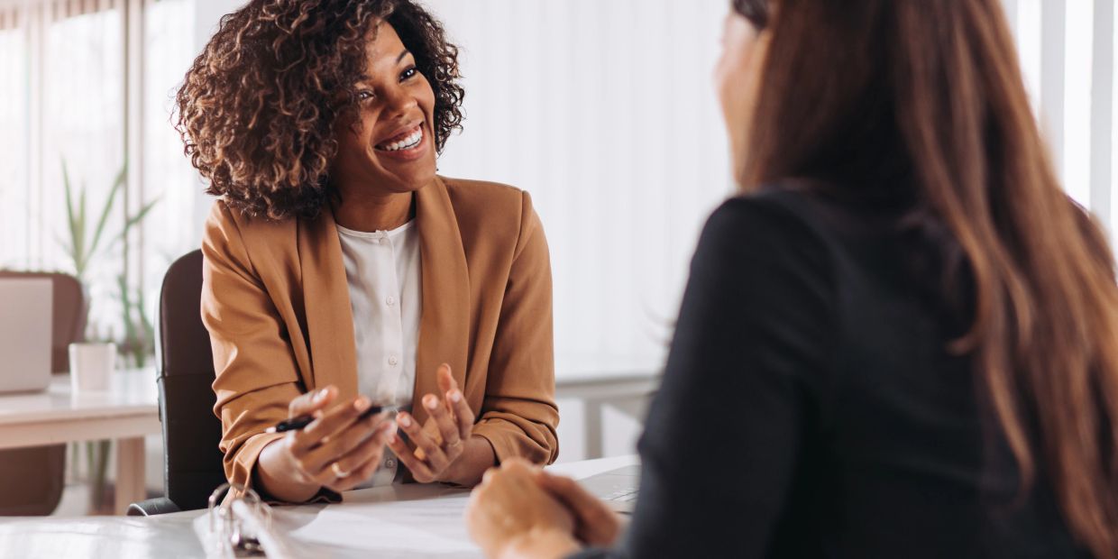 Two women engaged in a friendly office conversation.