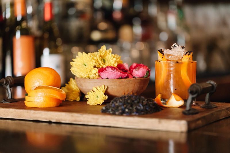 A colorful handcrafted alcoholic rum cocktail with ingridients such as oranges, tumeric and black sesame seeds