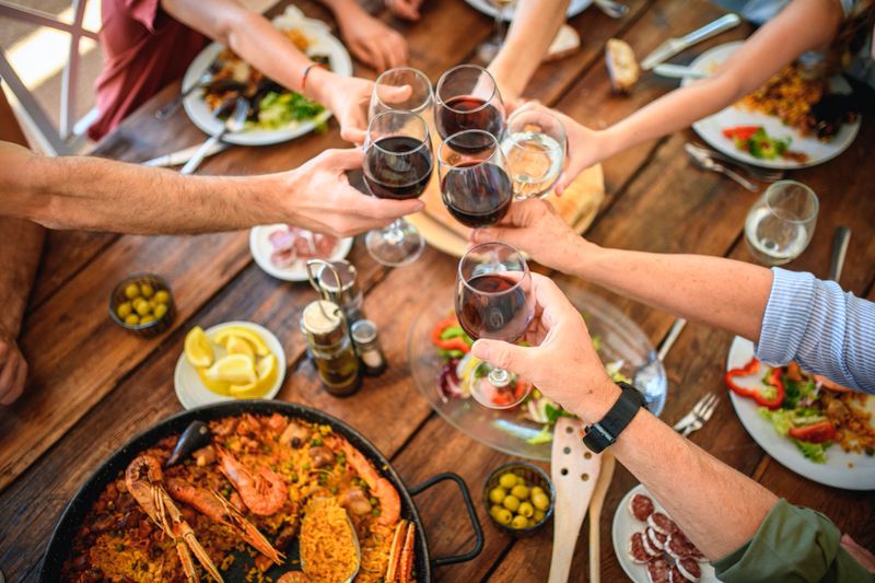 High angle view of three-generation Spanish family toasting with wine and water as they begin traditional midday meal of paella on weekend.