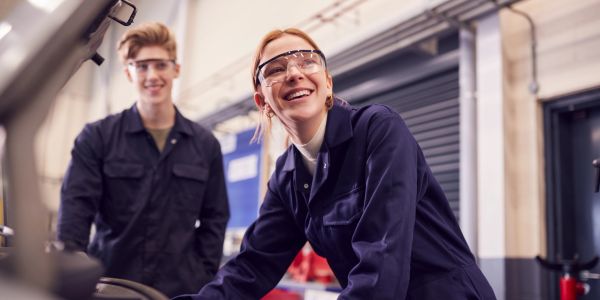 Dos jóvenes con gafas de seguridad trabajando en taller.