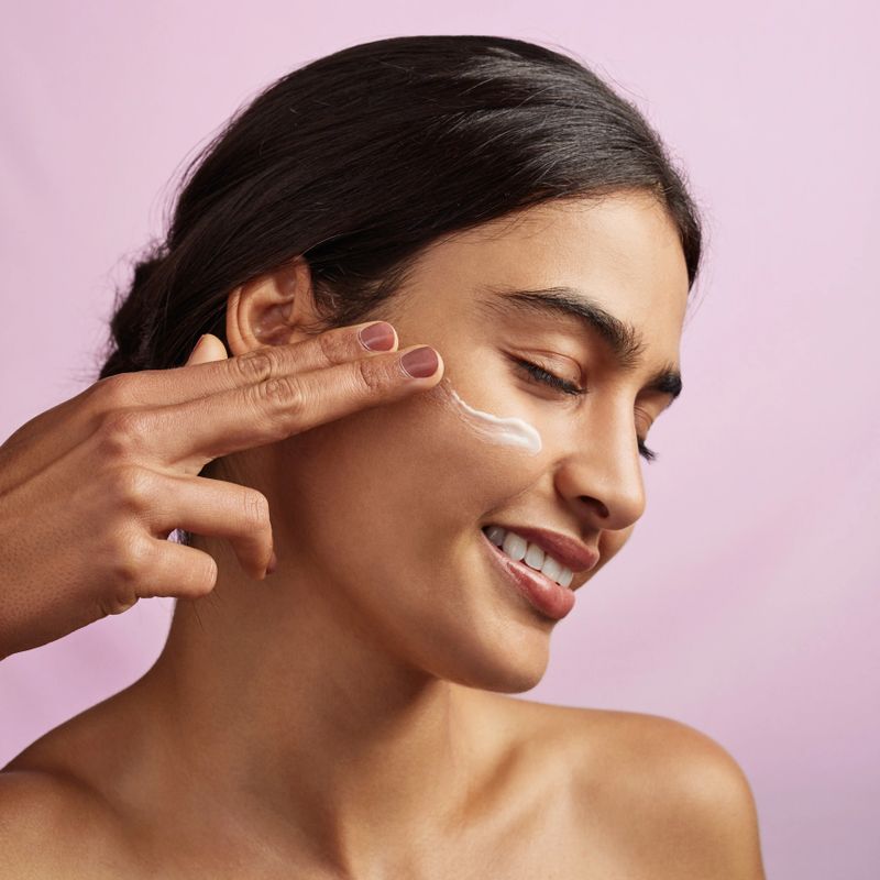Studio shot of a beautiful young woman applying moisturizer to her face