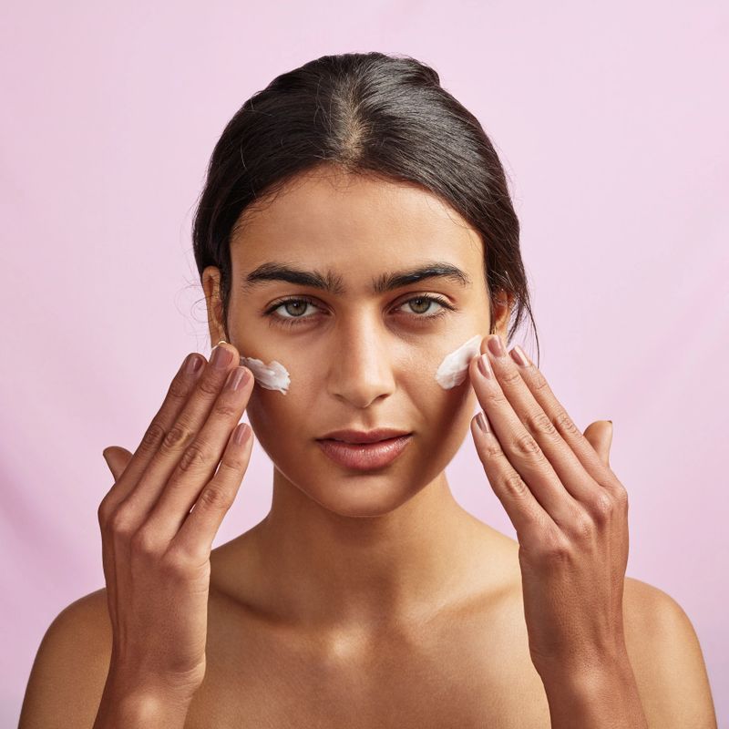 Studio shot of a beautiful young woman applying moisturizer to her face