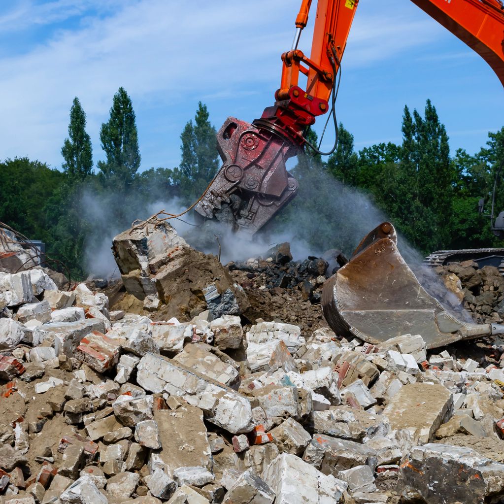Excavator demolishing concrete rubble with dust rising.