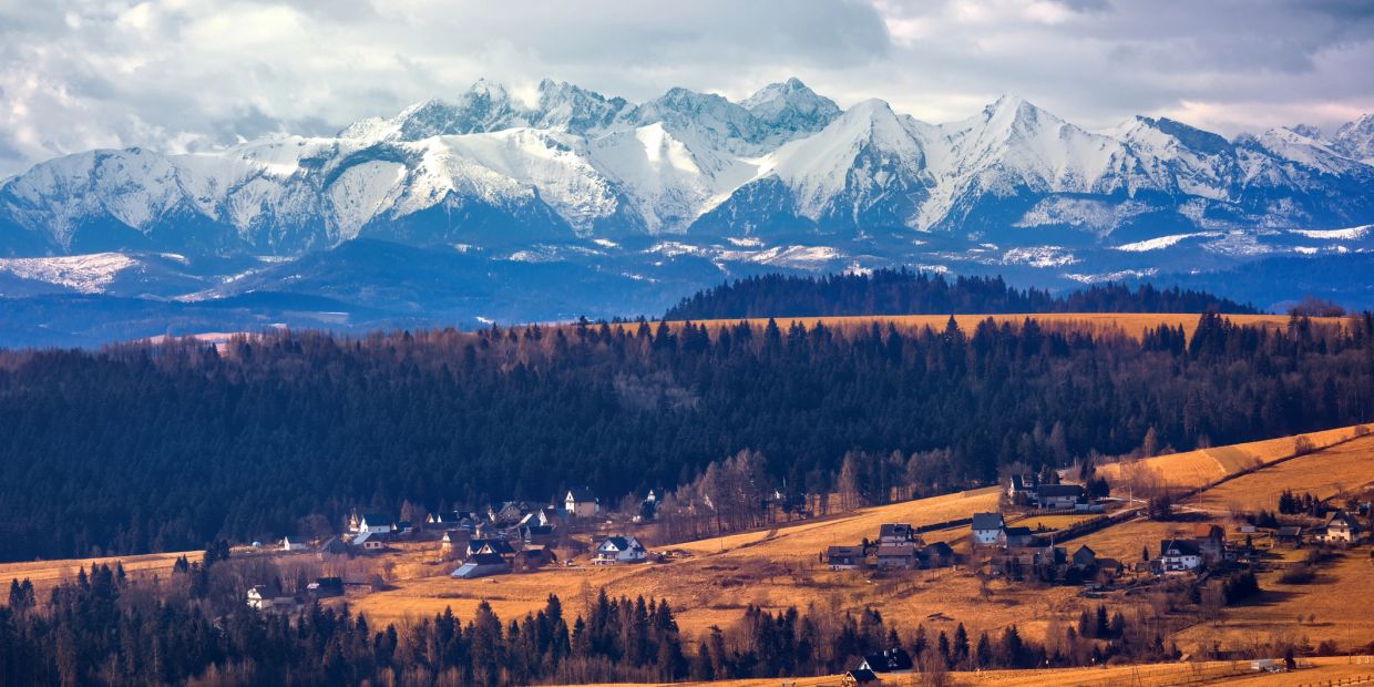 Snow-capped mountains over a small village and forest.