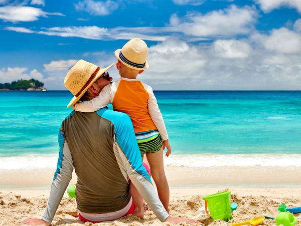 Father and son enjoying a sunny day at the beach with toys scattered in the sand.