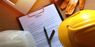 Construction contract with helmets and gloves on table.
