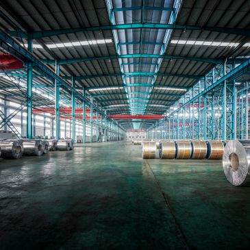 Spacious industrial warehouse with metal coils and high blue shelving racks.