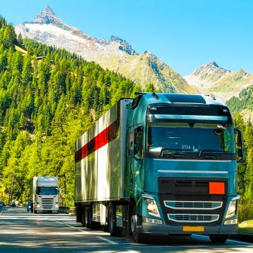 Two large trucks driving on a mountain road surrounded by trees.
