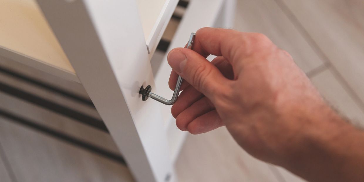 Hand tightening a screw with a hex key on white furniture.