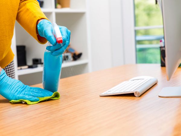 Professional office cleaner wiping down a computer desk.