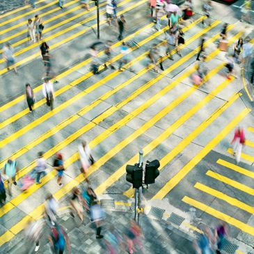 Blurred motion of pedestrians crossing a busy street with yellow crosswalk lines.