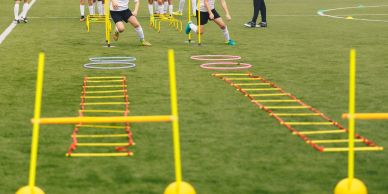 Athletes training agility with ladders and hurdles on a field.