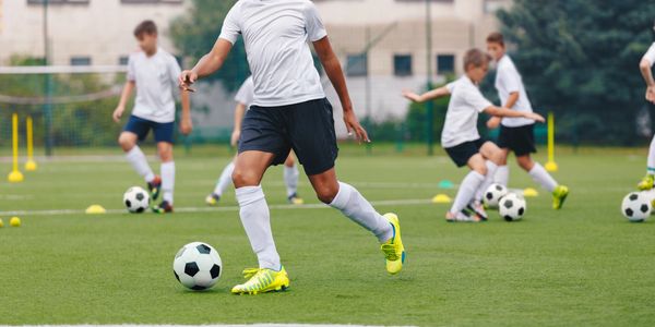 Kids practicing soccer drills on a green field wearing white shirts and bright cleats.