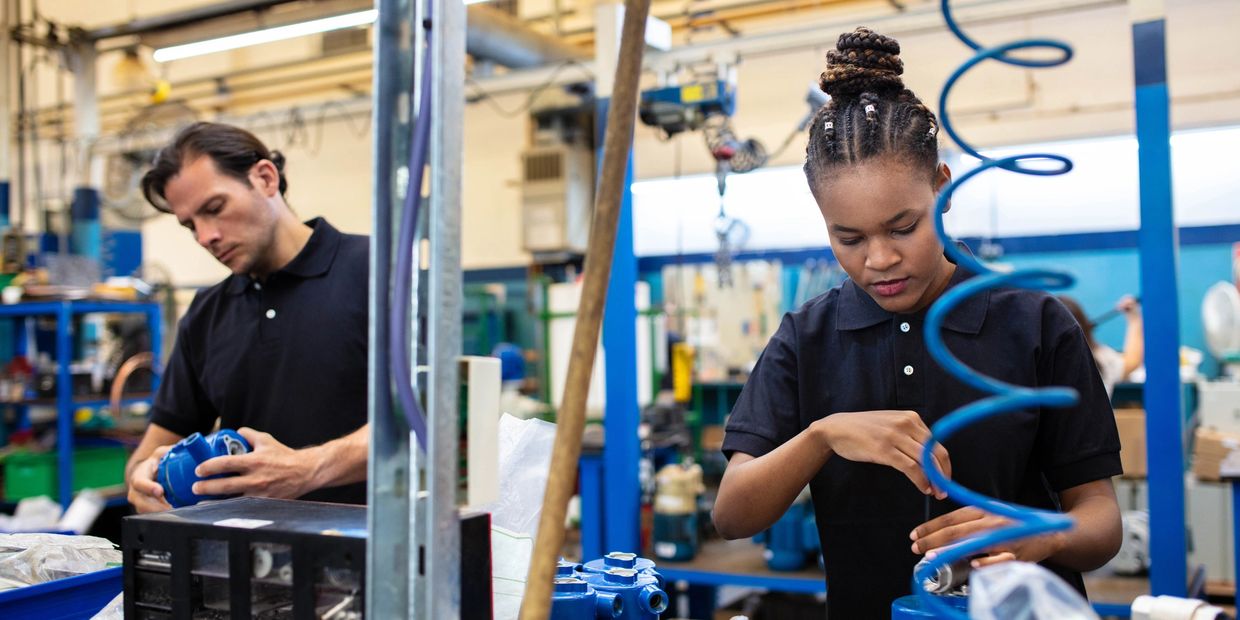 Two factory workers assembling blue mechanical parts.