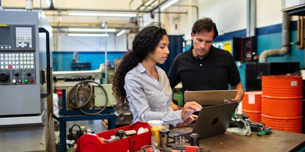 Two engineers collaborating on a laptop in a workshop.