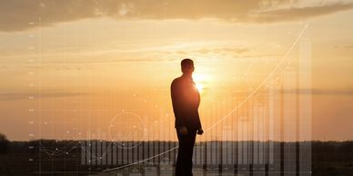 Silhouette of a businessman with rising financial charts at sunset.