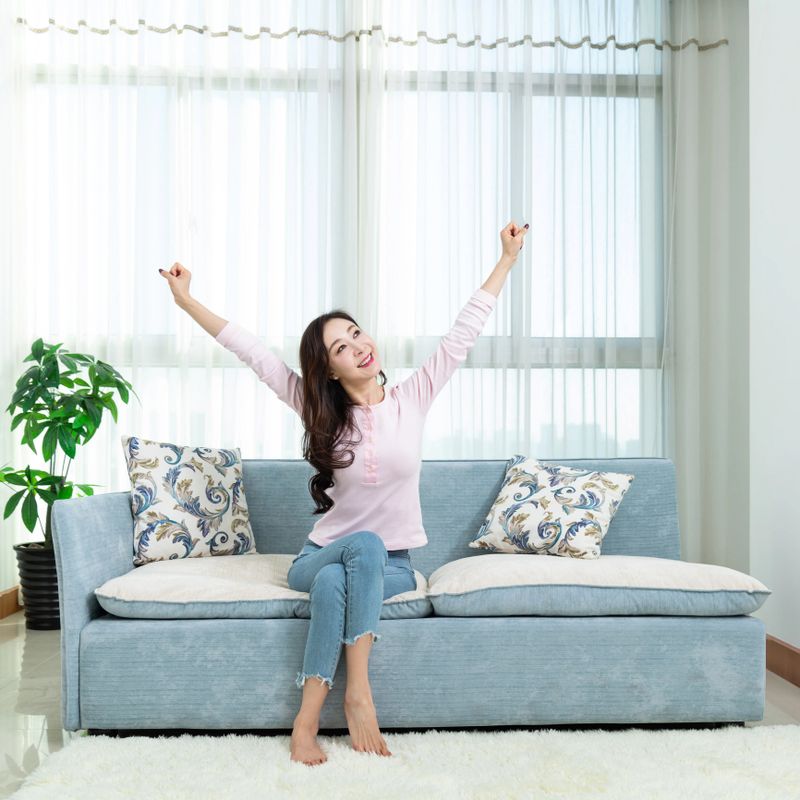Beautiful woman sitting on sofa and arms raised.