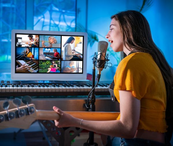 Woman singing and playing guitar during video call music session.