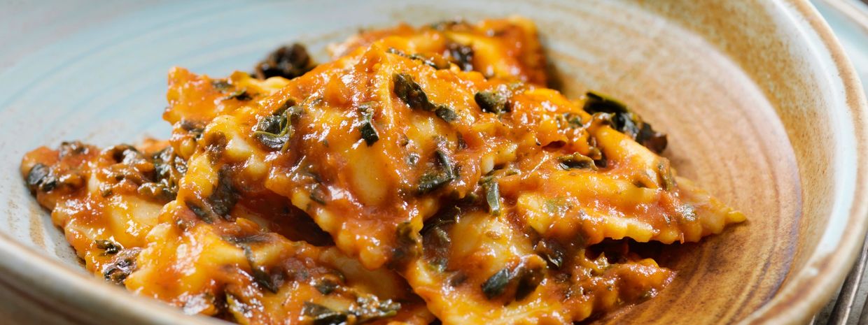 A rustic Italian meal with pasta, pizza, bread, and decorative blue bowls on a wooden table.