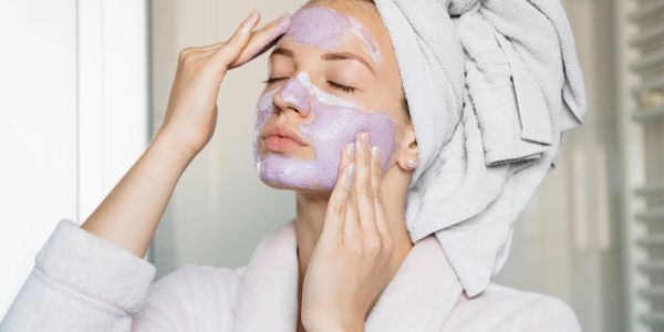 Woman applying a purple facial mask with a towel wrapped on her head.