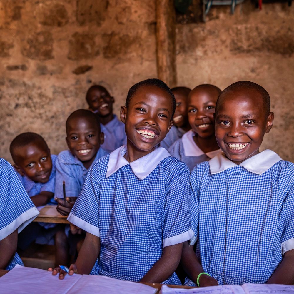 Smiling children in blue checkered school uniforms in a classroom.