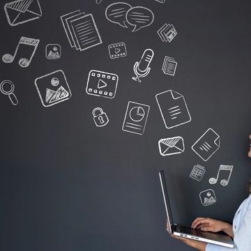 Woman using laptop with digital media icons floating above.