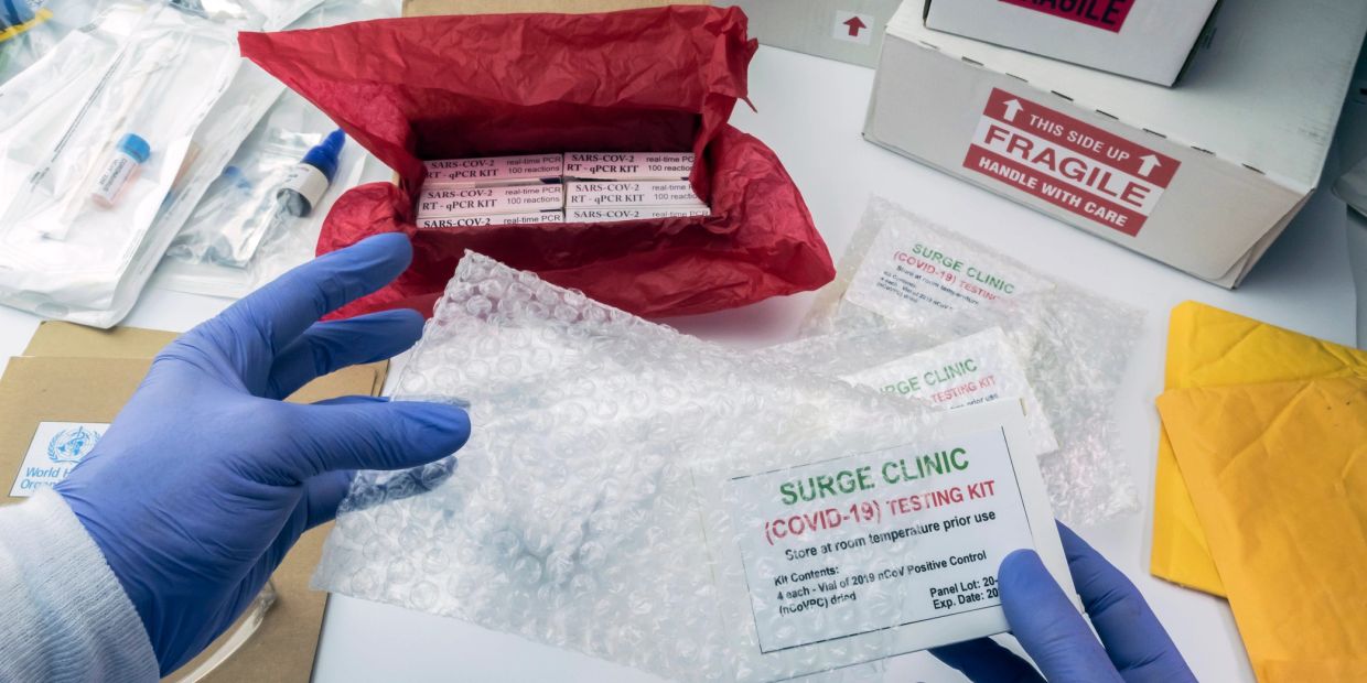 Person handling COVID-19 testing kits with gloved hands.
