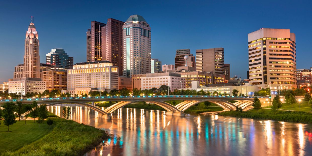 City skyline at dusk with illuminated buildings and bridge.