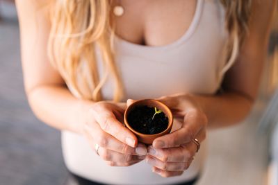 Woman holding a small pot with a sprouting seedling.