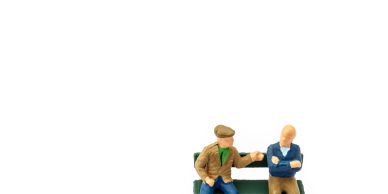 Miniature figurines of two men sitting and talking on a bench.