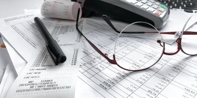 Eyeglasses, a pen, and documents with numbers on a desk.
