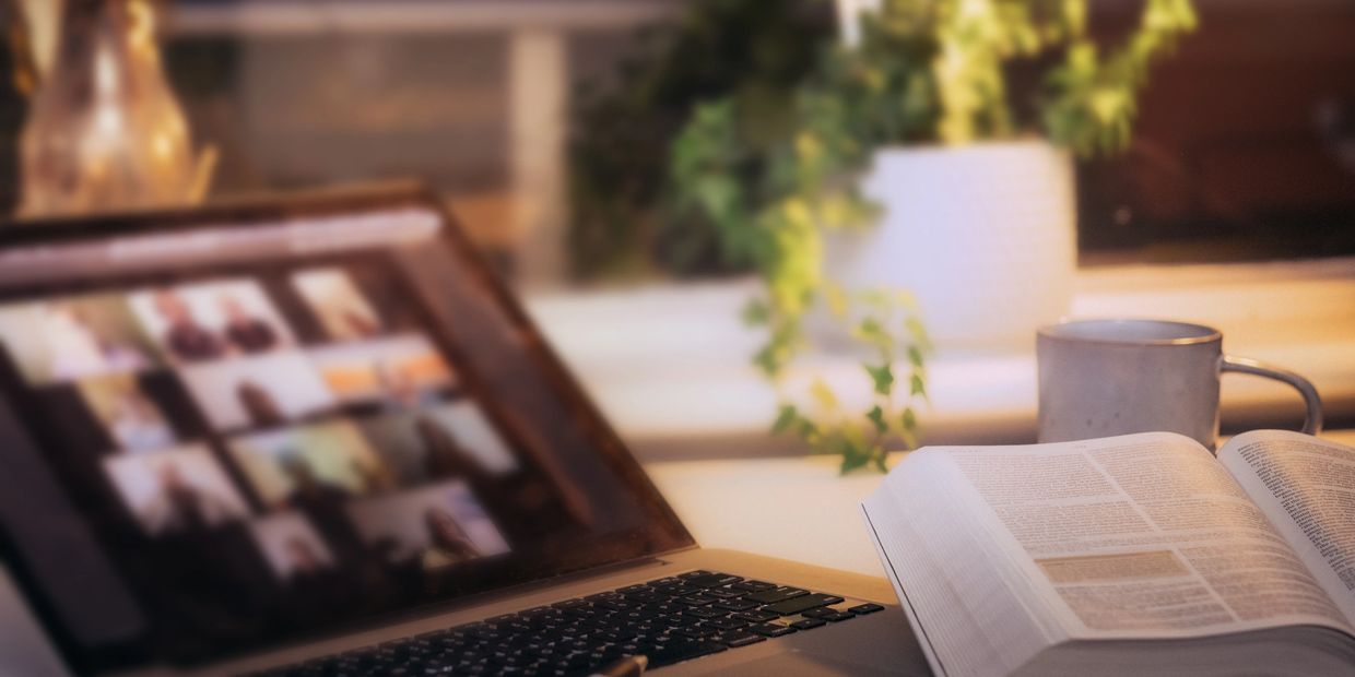 Cozy study setup with laptop, open book, and coffee mug on a desk near a plant.