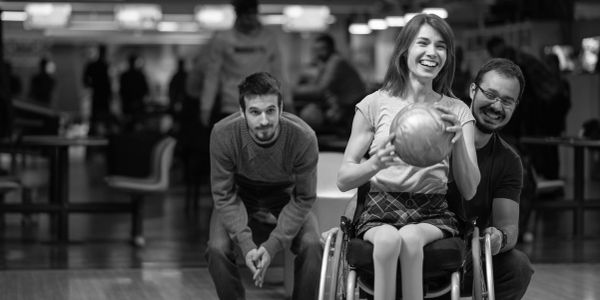 Smiling woman in wheelchair holding bowling ball with friends.