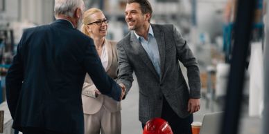 Three professionals shaking hands in an industrial setting with smiles.
