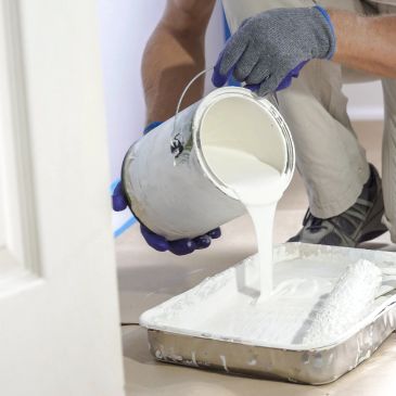 Person pouring white paint into a tray for painting.