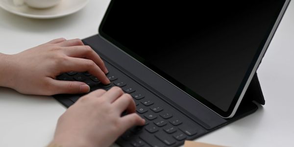 Hands typing on a tablet keyboard with a cup of coffee nearby.